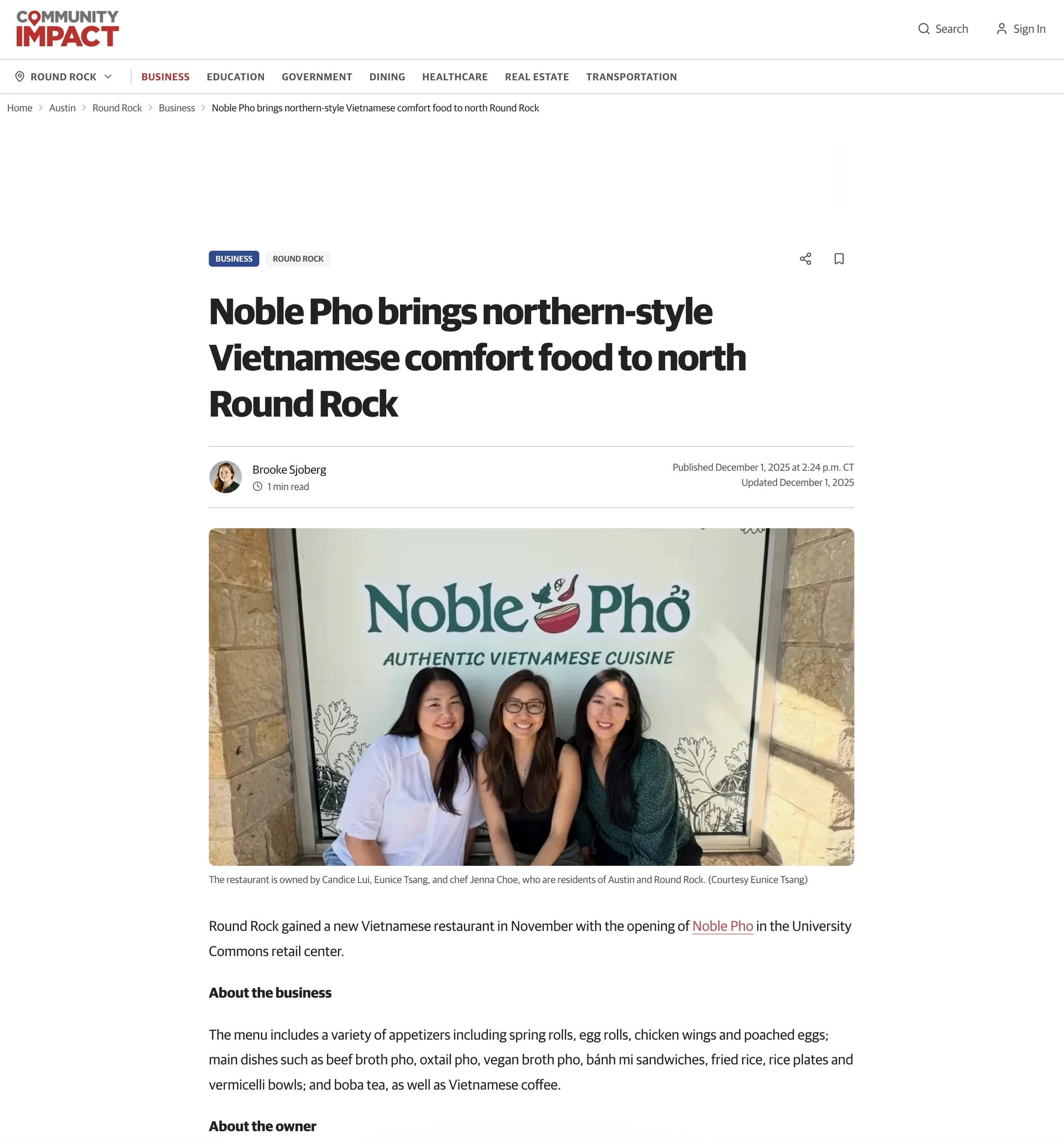 Three women smiling and standing in front of a sign that reads 'Noble Pho' with a subtitle 'Authentic Vietnamese Cuisine'. The women are dressed in professional attire and are standing indoors in front of a decorative wall next to a door.