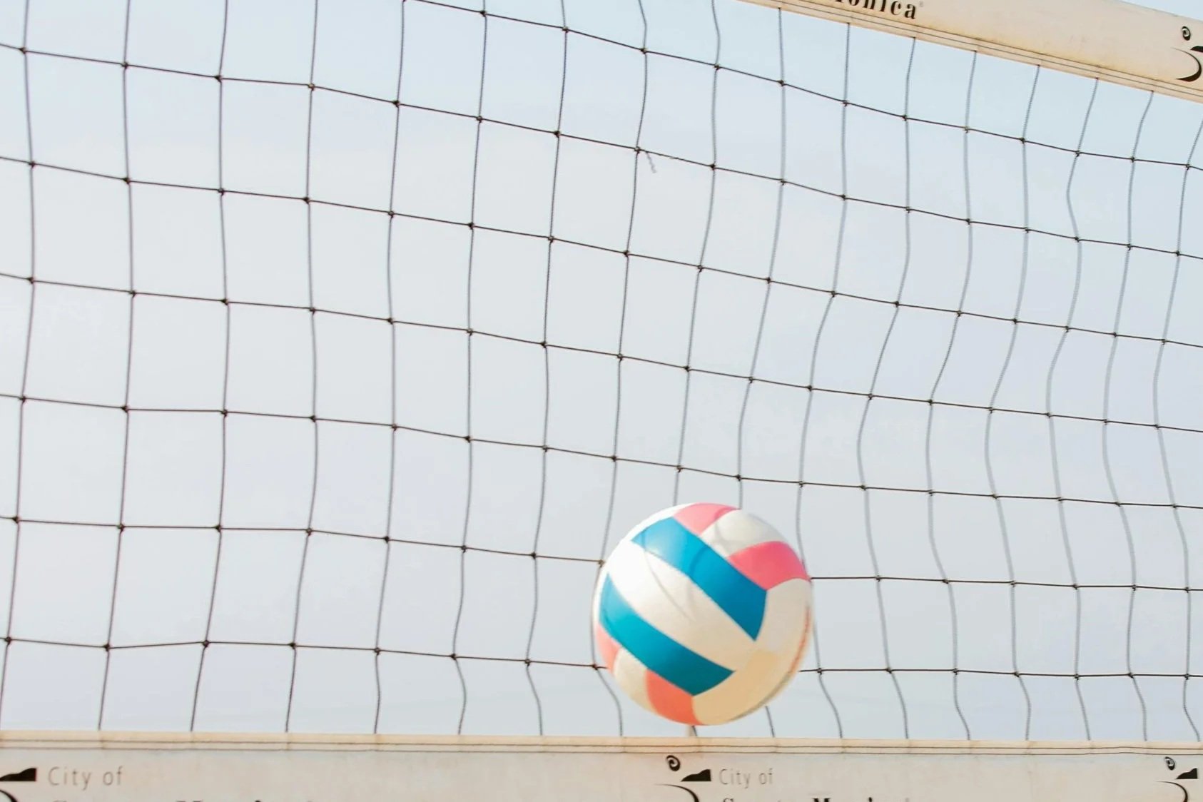A volleyball in mid-air over a volleyball net against the sky.