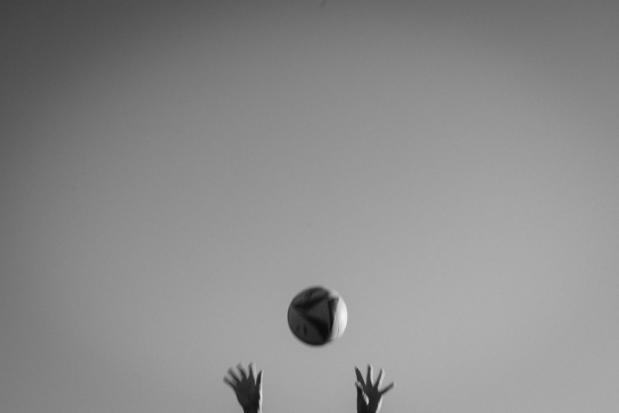 Two hands reaching upward towards a ball in black and white.