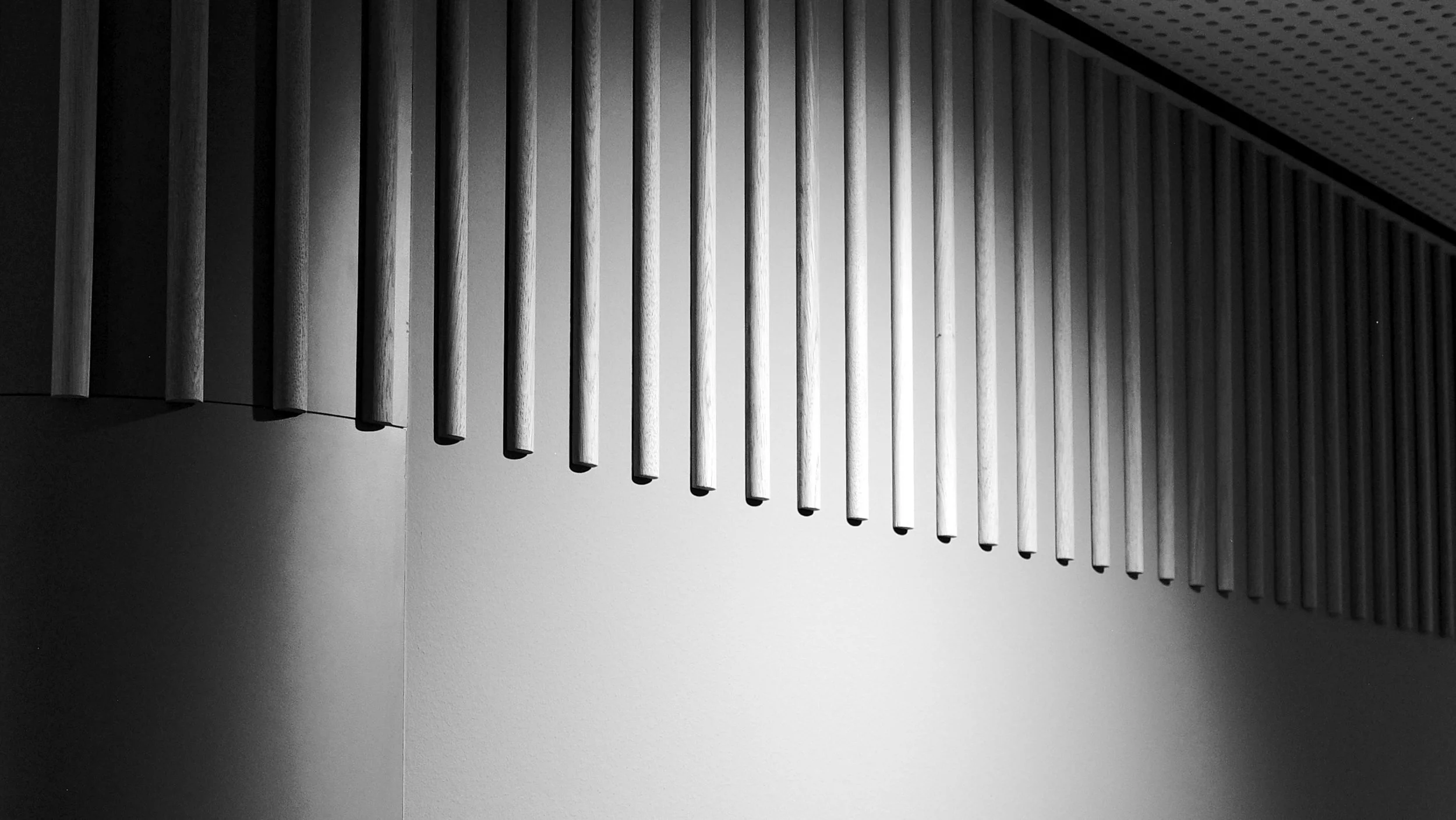 Schwarz-Weiß-Foto unserer modernen Innenarchitektur mit parallelen, vertikalen Holzleisten an der Wand und einer abgerundeten weißen Wand.
