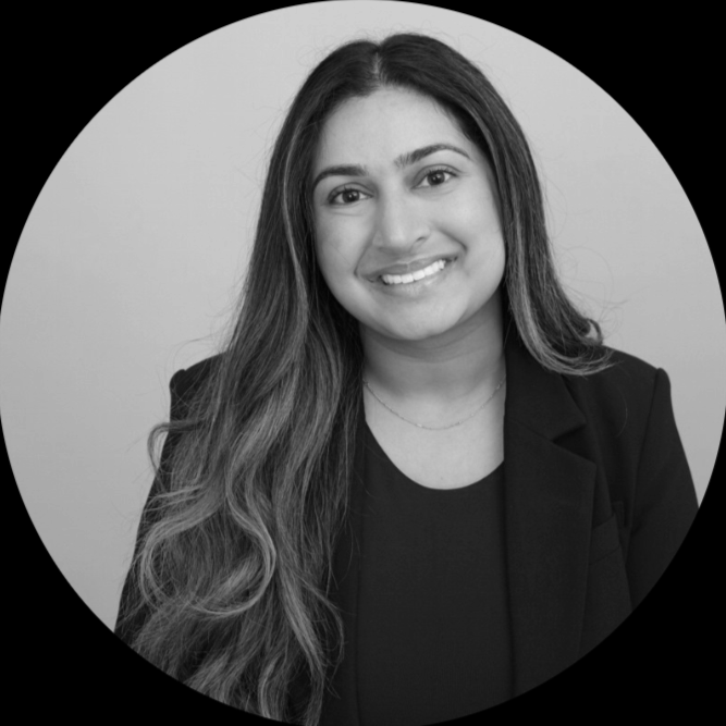 Black and white headshot of a young woman with long wavy hair, smiling, wearing a blazer and a necklace.