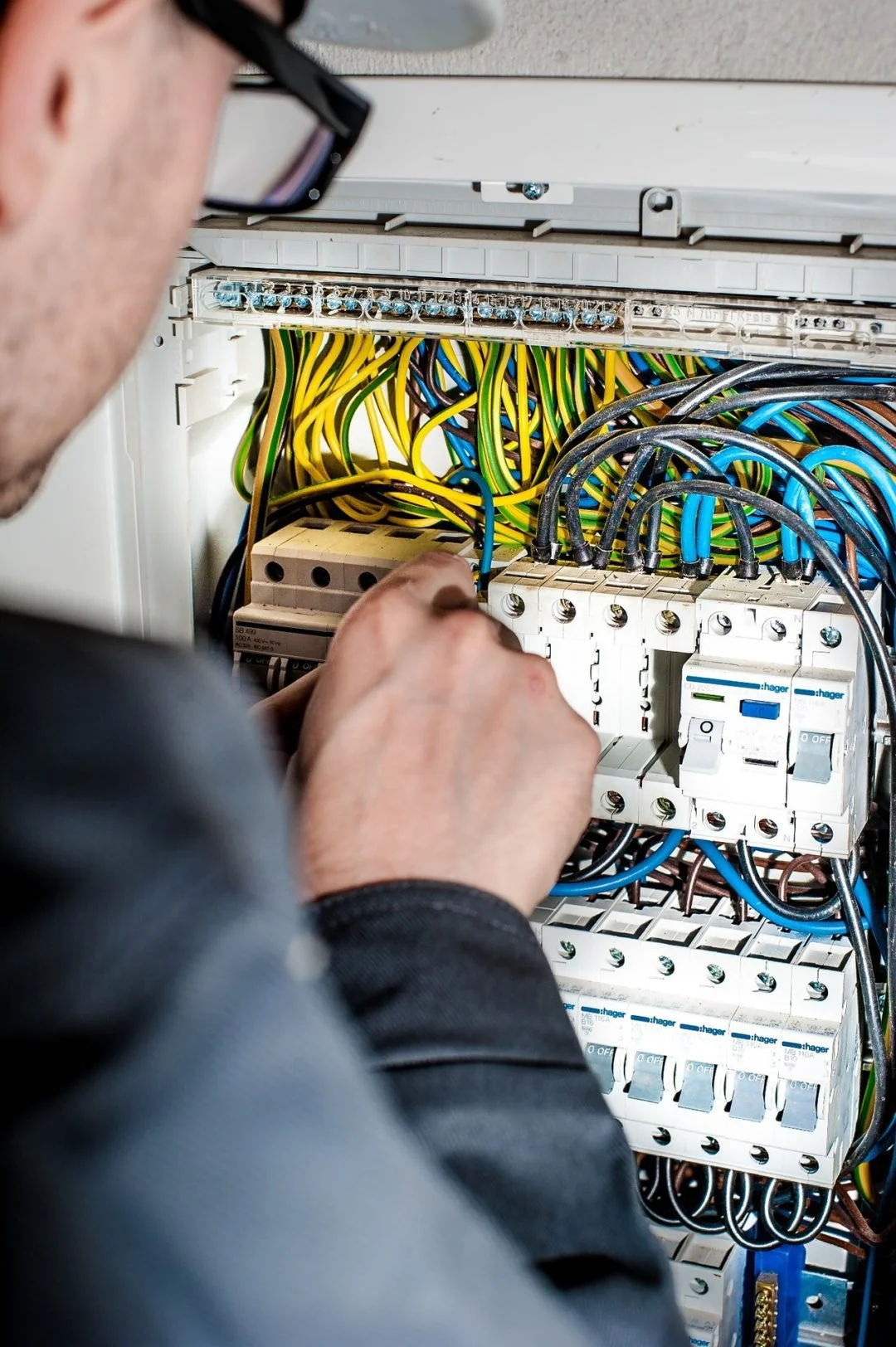 Un technicien manipule des fils et des disjoncteurs dans un tableau électrique.