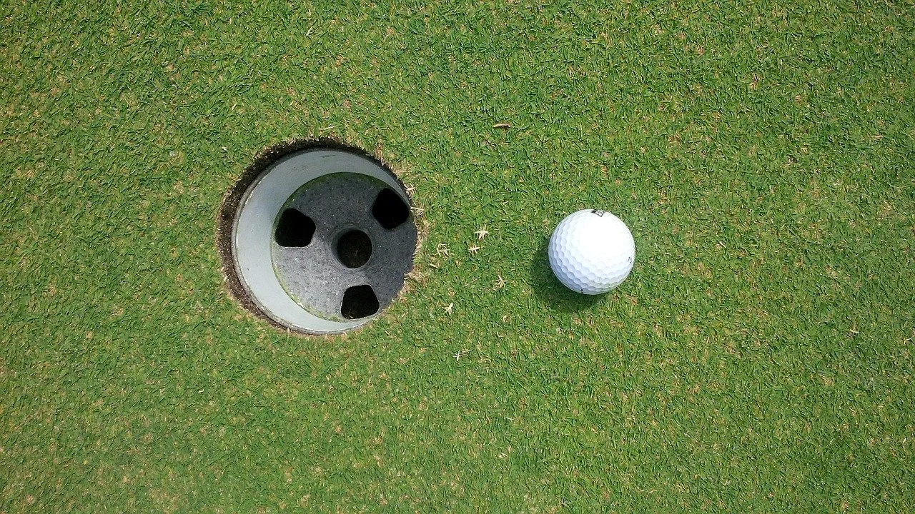 Close-up of a golf hole on a putting green with a golf ball near the hole.