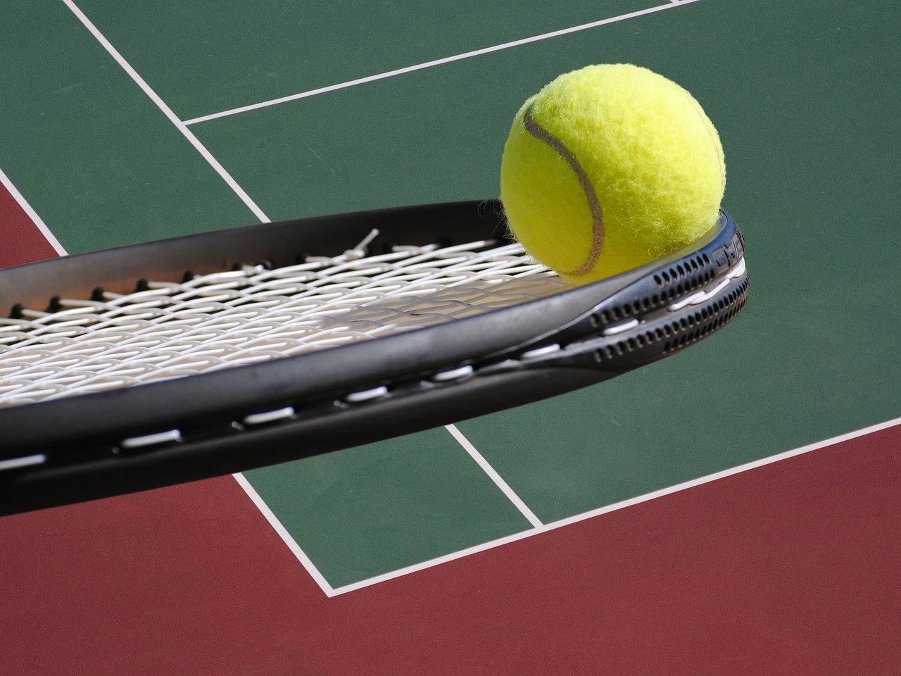 A tennis ball resting on a tennis racket at the edge of a tennis court.