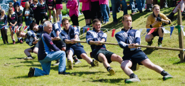 People participating in a tug-of-war game outdoors with spectators watching.