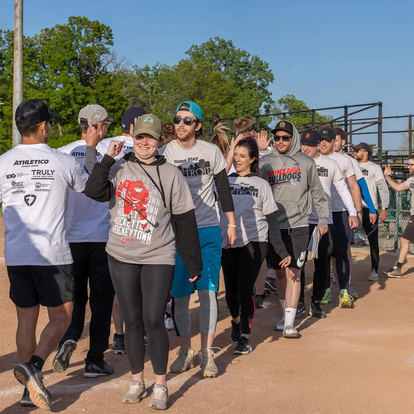 A group of people wearing sports shirts are giving each other high fives on a sports field, with some smiling and others appearing happy.