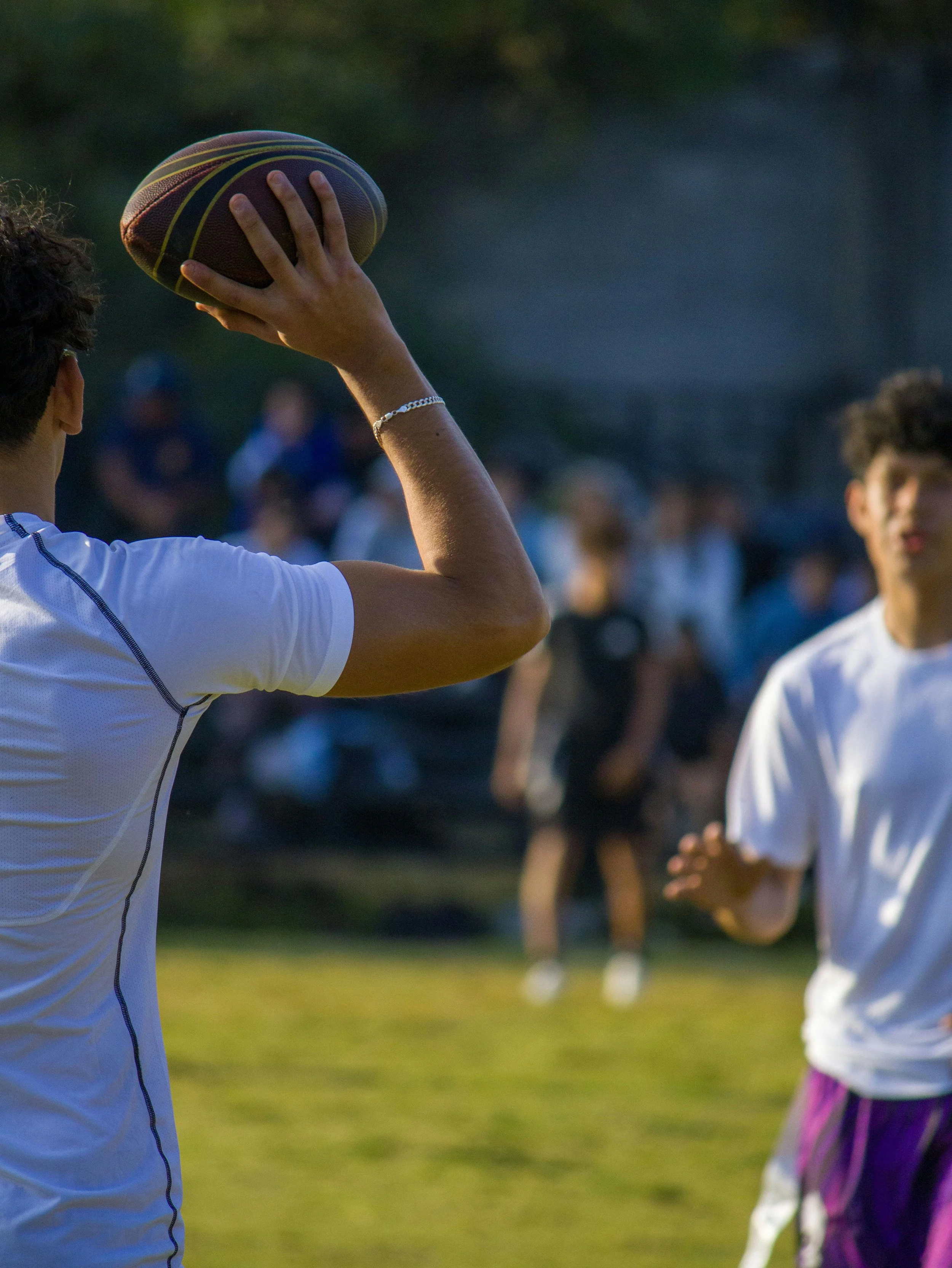 A person holding a football ready to throw while others are in the background, outdoors during the daytime.