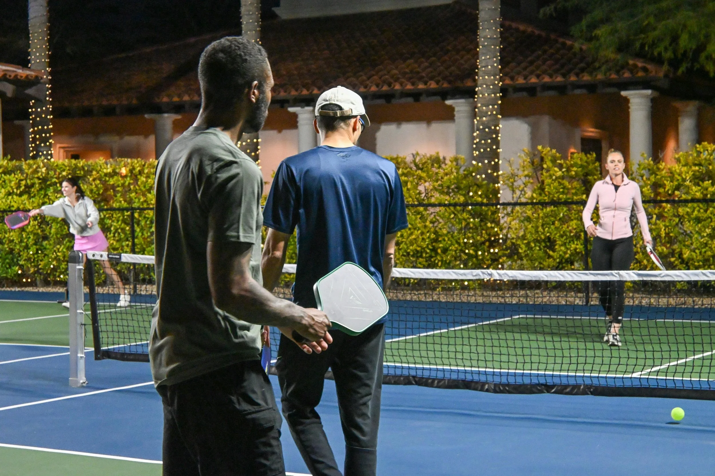 People playing pickleball on an outdoor court at night.