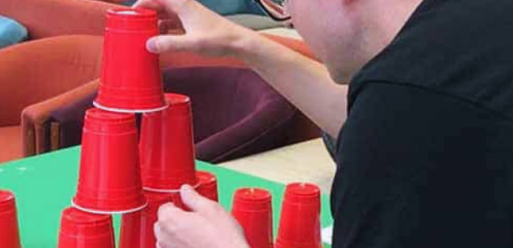 Person stacking red plastic cups in a pyramid on a green table.