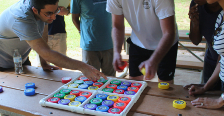 Group of people playing a game of Twister outdoors on a wooden table.
