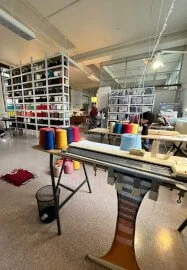 Interior of a knitwear studio with shelves of colourful thread spools, work tables, and vintage knitting machines.