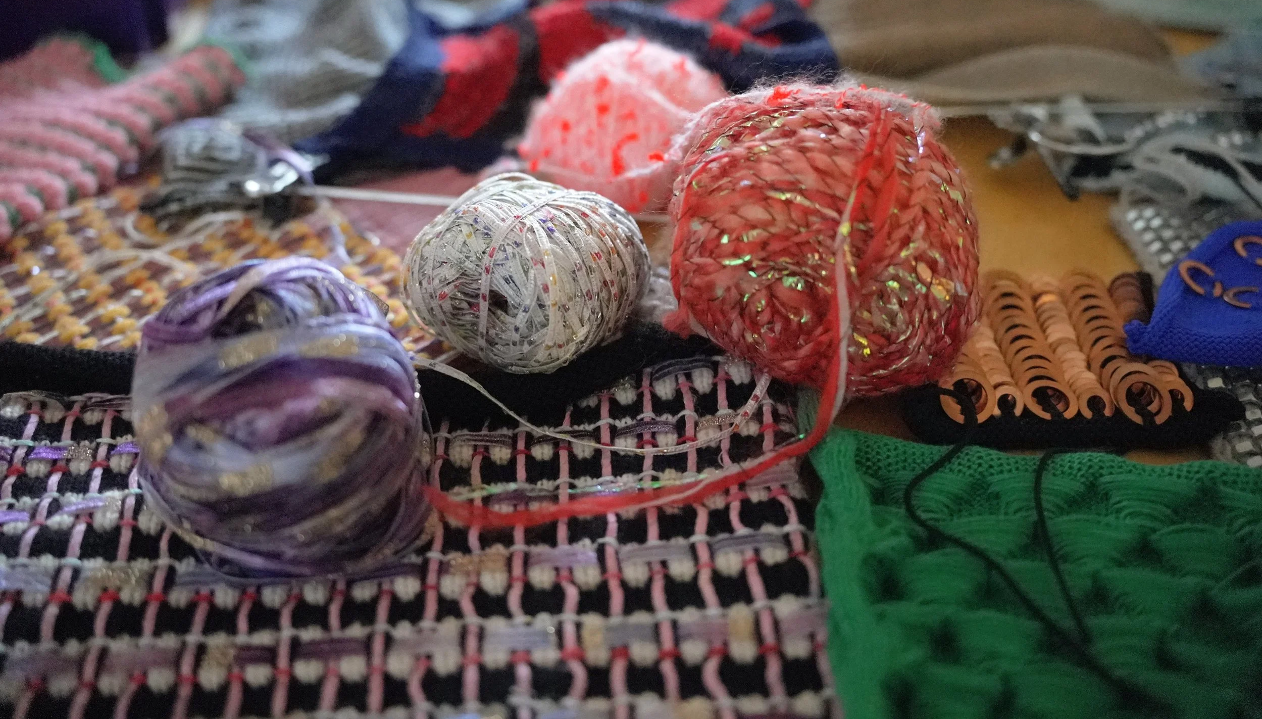 Various balls of yarn and knitting and crochet supplies spread across a woven fabric surface.