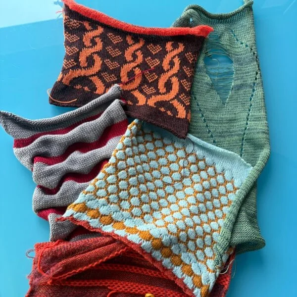 Several colourful, handmade knitted swatches with various patterns, including stripes, honeycomb, and distressed details, lie on a blue surface.