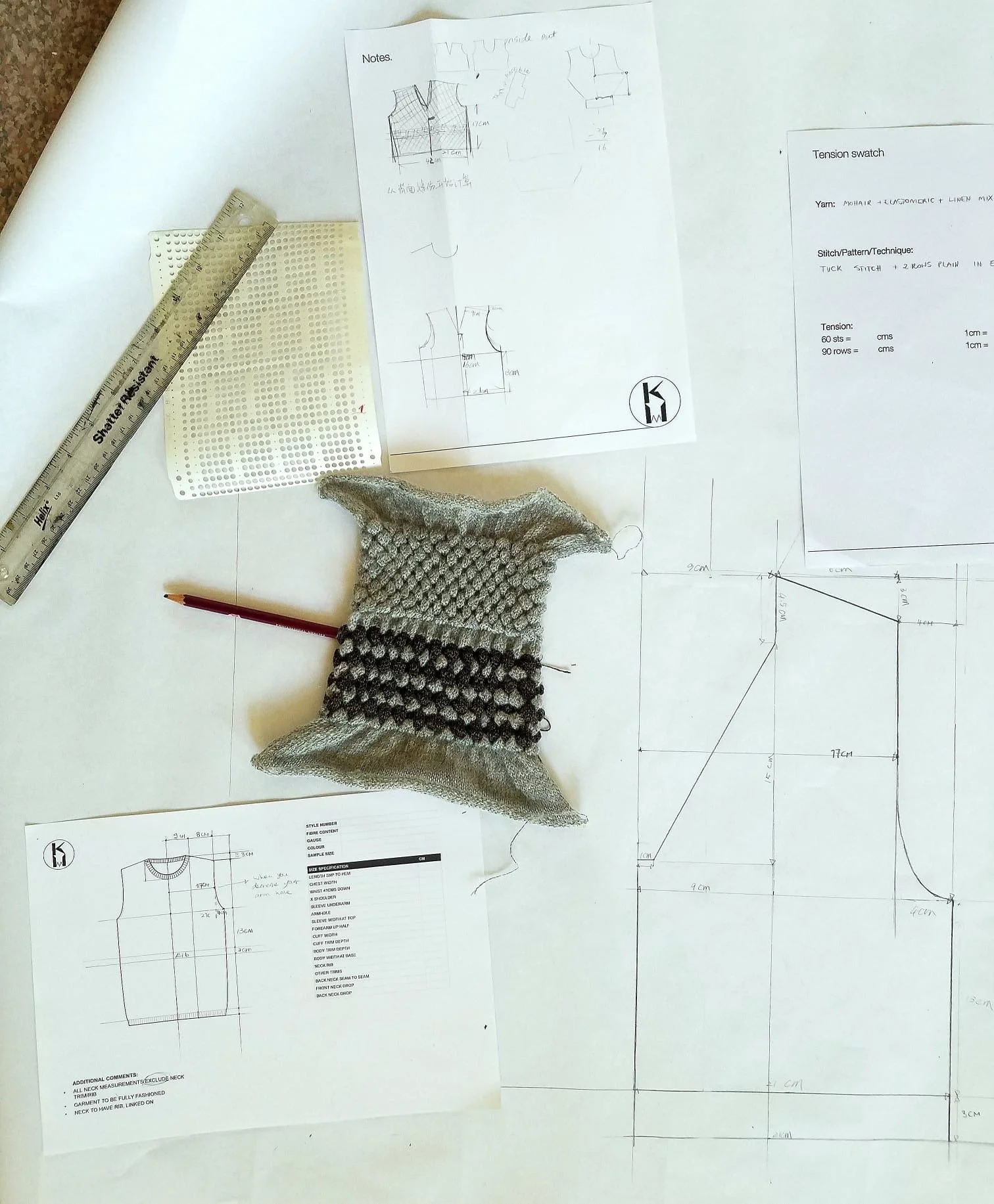 Flat lay view of pattern design sketches, technical drawings, and notes for knitwear projects on white pattern paper, with a clear ruler, a knitted fabric sample, and a pencil placed on top.