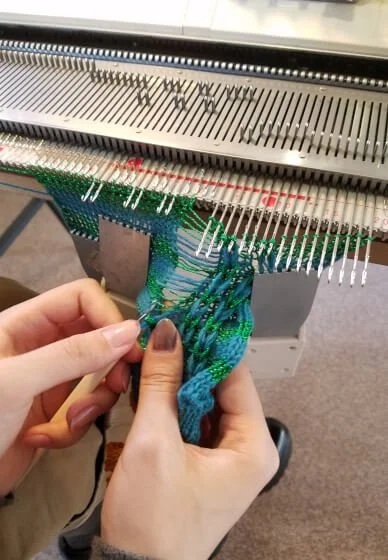 Close-up of hands working on a knitting machine with colorful yarns.