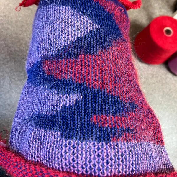 Close-up of a colourful fabric, striped and woven with purple, red, black, and pink colours, showing a textured knit pattern.