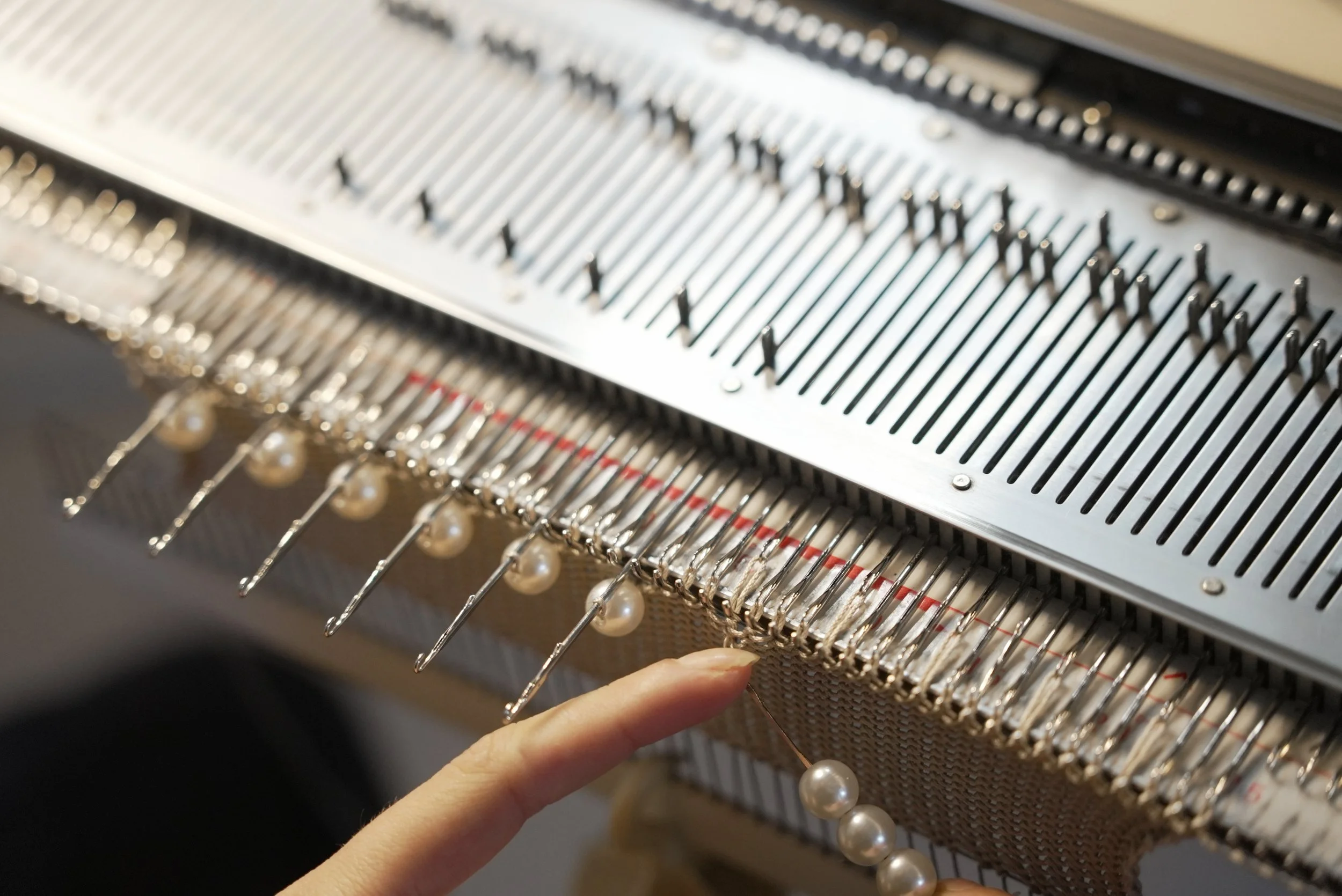 A close-up of a person adding pearl-like beads to a knitting machine.