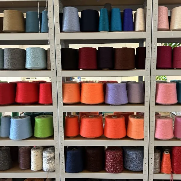 Shelving unit filled with spools of multicoloured threads and yarns organised by colour and fibre makeup.