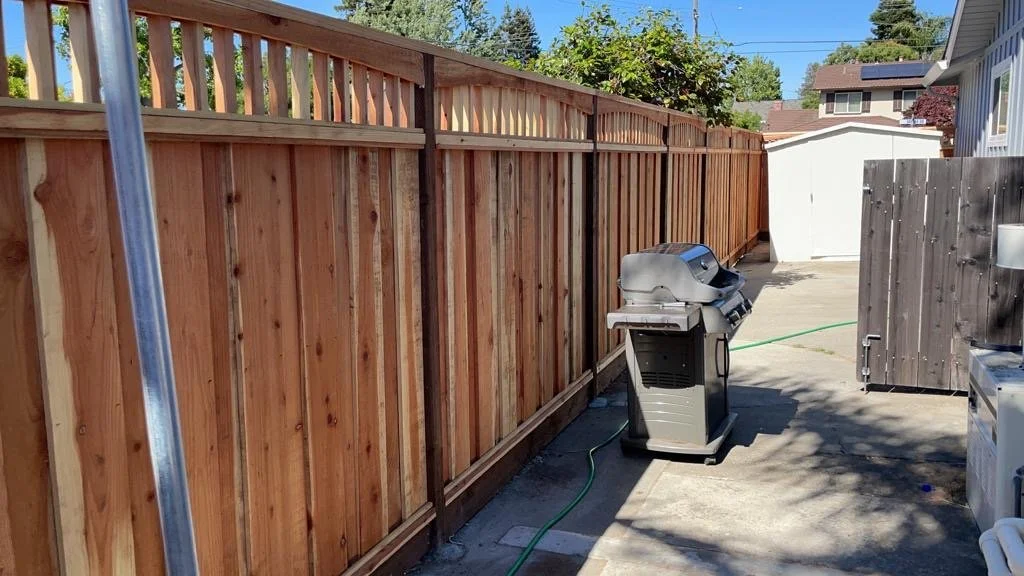 Backyard with newly installed wooden fence, a gas grill, a white shed, and a small brown storage box.