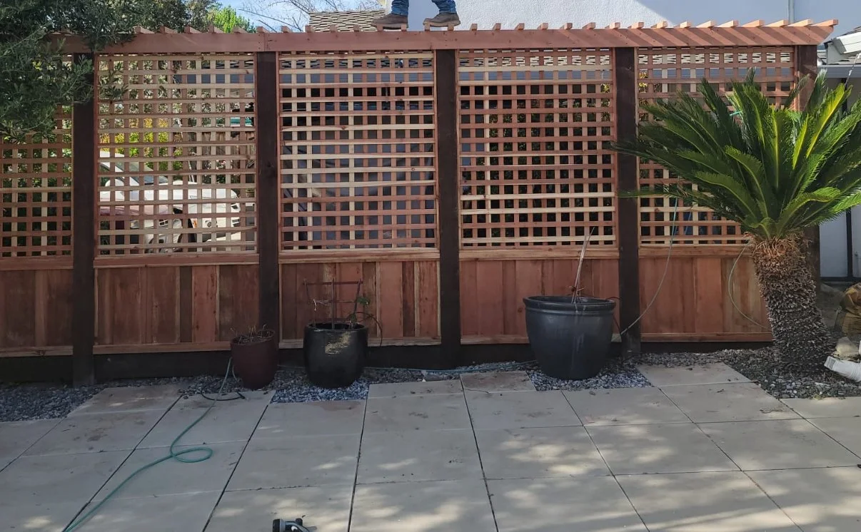 New wooden privacy fence being installed in a backyard with potted plants and patio tiles.
