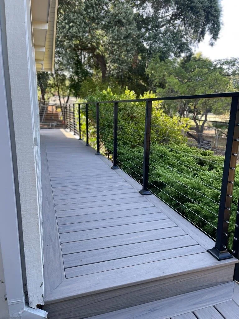 A view of a wooden balcony with black metal railing overlooking trees and greenery.