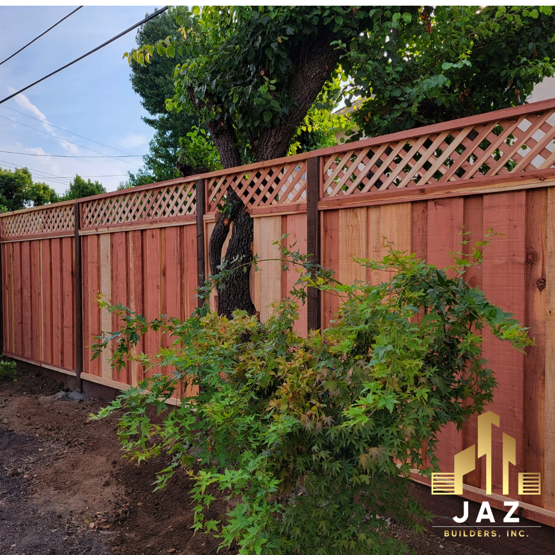 New wooden privacy fence installed beside a tree with green foliage, with a clear blue sky in the background, logo of JAZ Builders, Inc. in the bottom right corner.