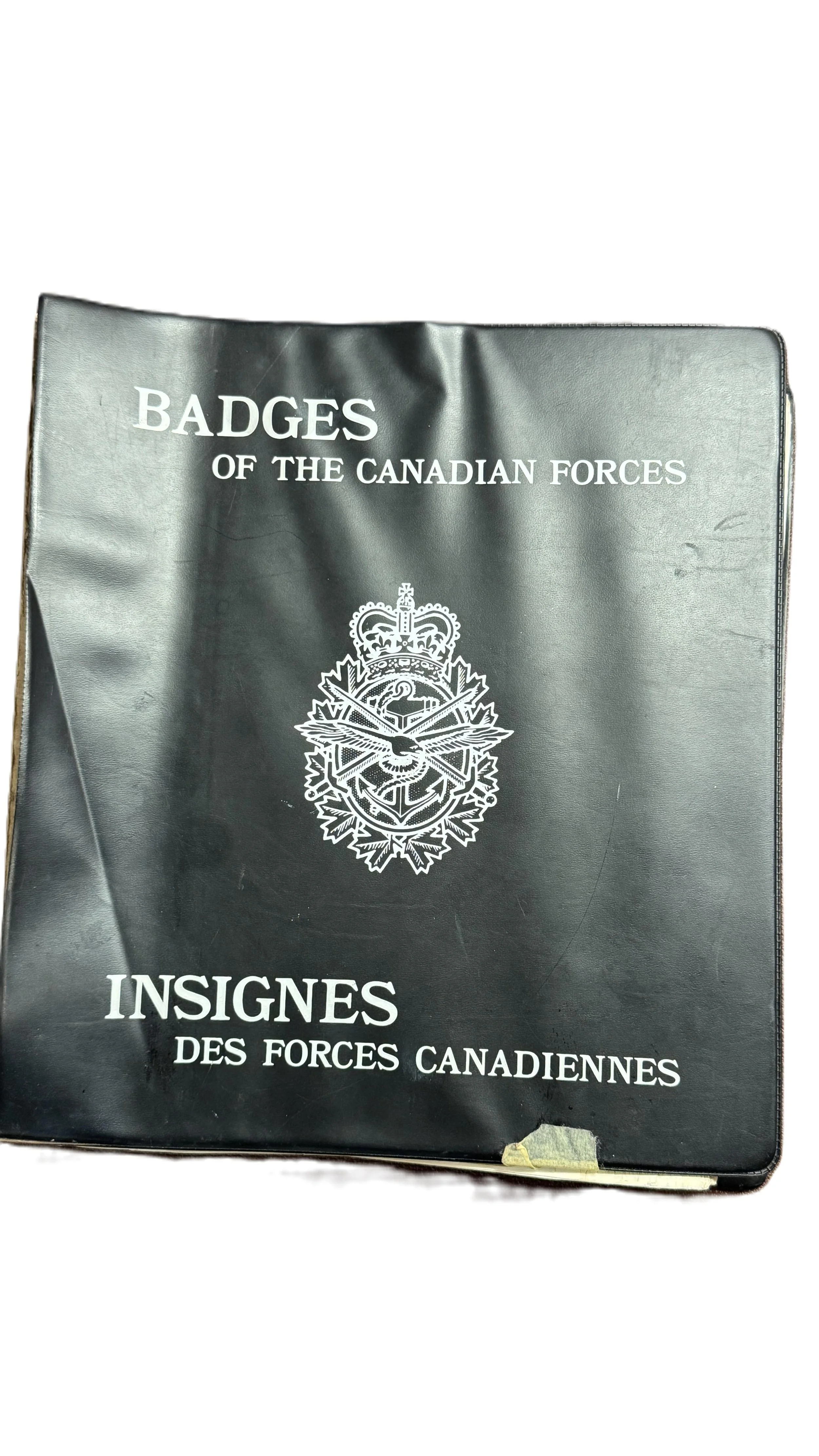 A black booklet titled "Badges of the Canadian Forces Insignes des Forces Canadiennes" with a white emblem and some wear at the bottom.