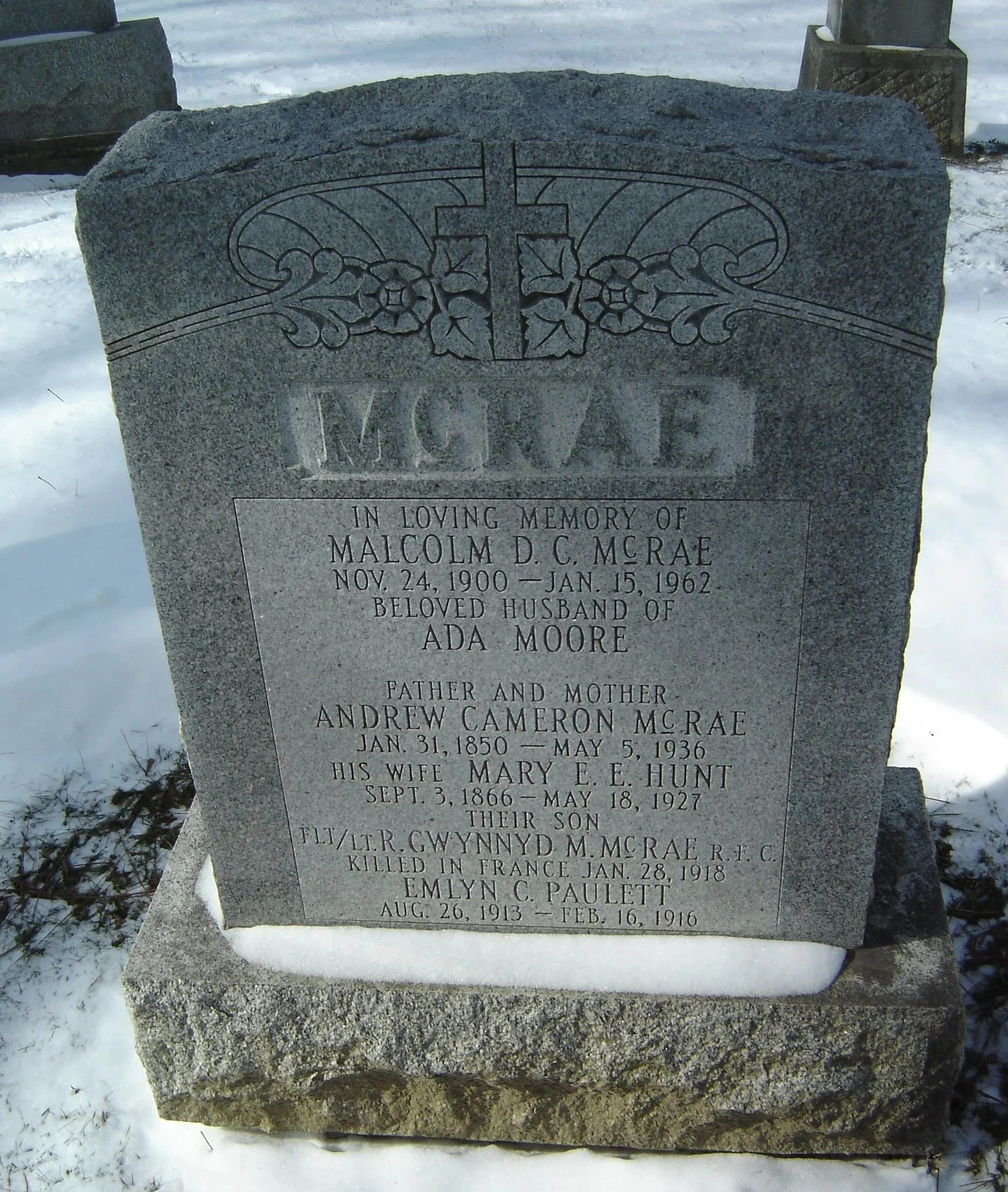 Gravestone with a cross and floral engravings, inscribed with the names and dates of Malcolm D.C. McRae, Ada Moore, Andrew Cameron McRae, Mary E.E. Hunt, R.Gwynydd M. McRae, and Emlyn C. Paulett.