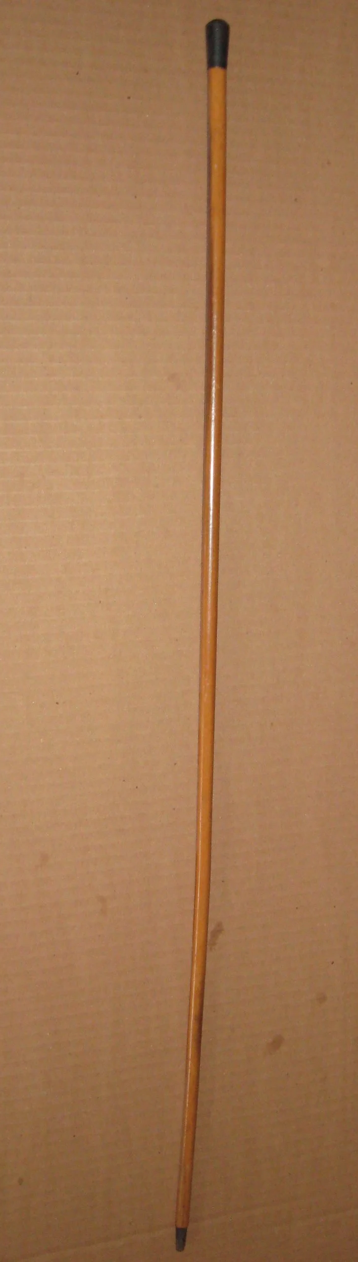 A long wooden stick with a black rubber tip at one end, leaning against a textured beige background.
