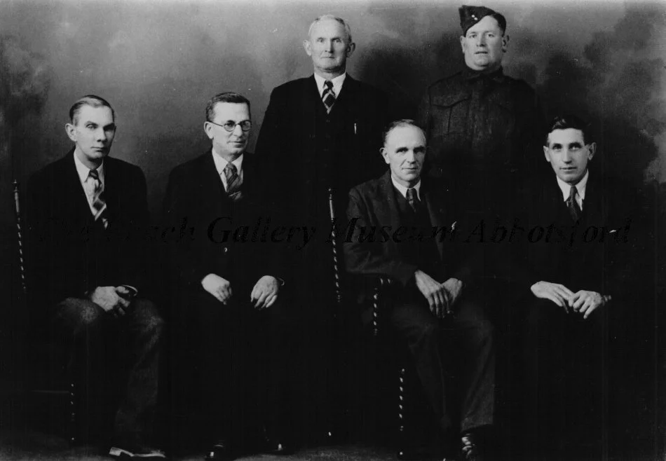 Black and white photo of seven men in formal and military attire, posing for a group portrait against a plain background.