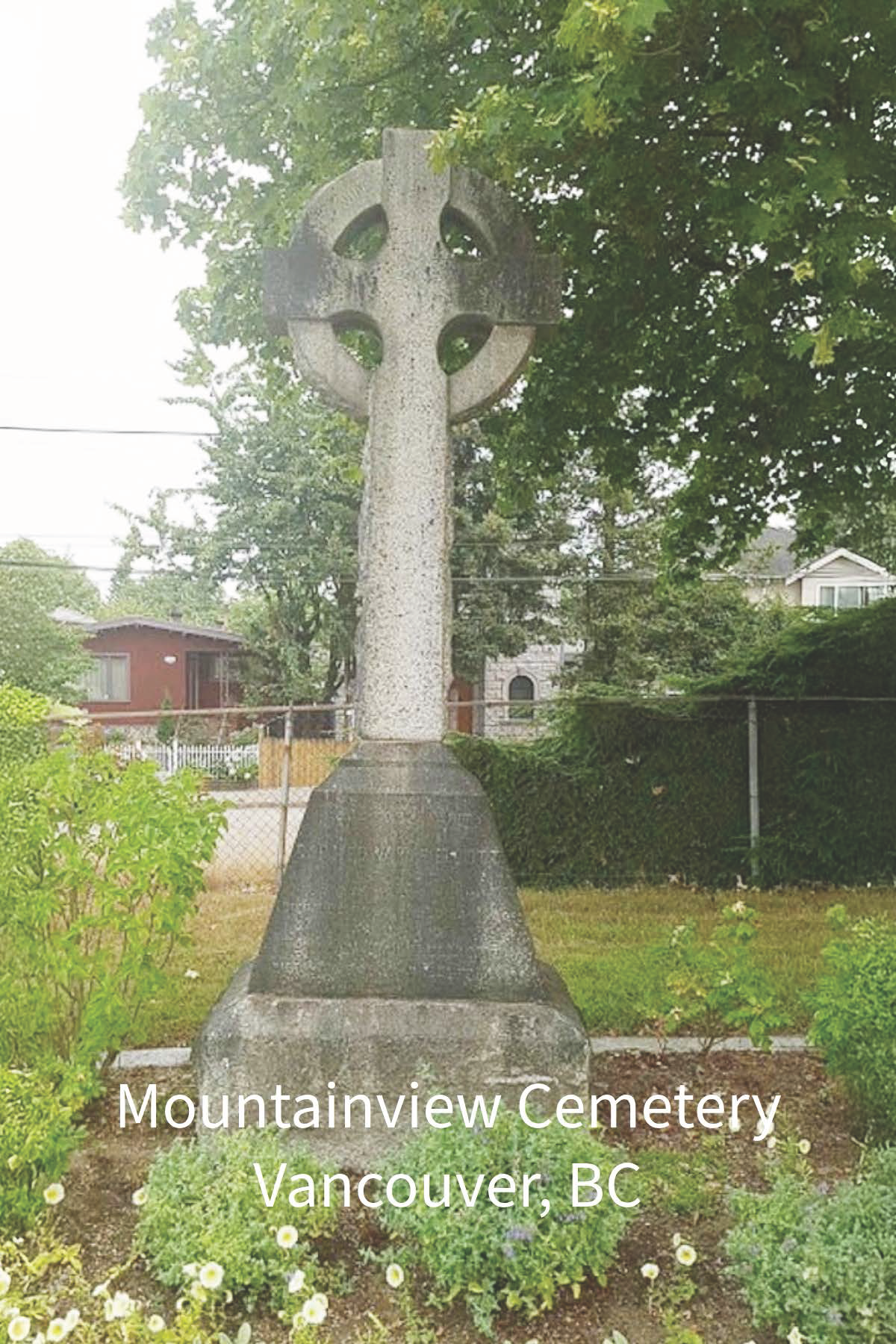 A stone Celtic cross monument at Mountainview Cemetery in Vancouver, BC, surrounded by green plants and trees.