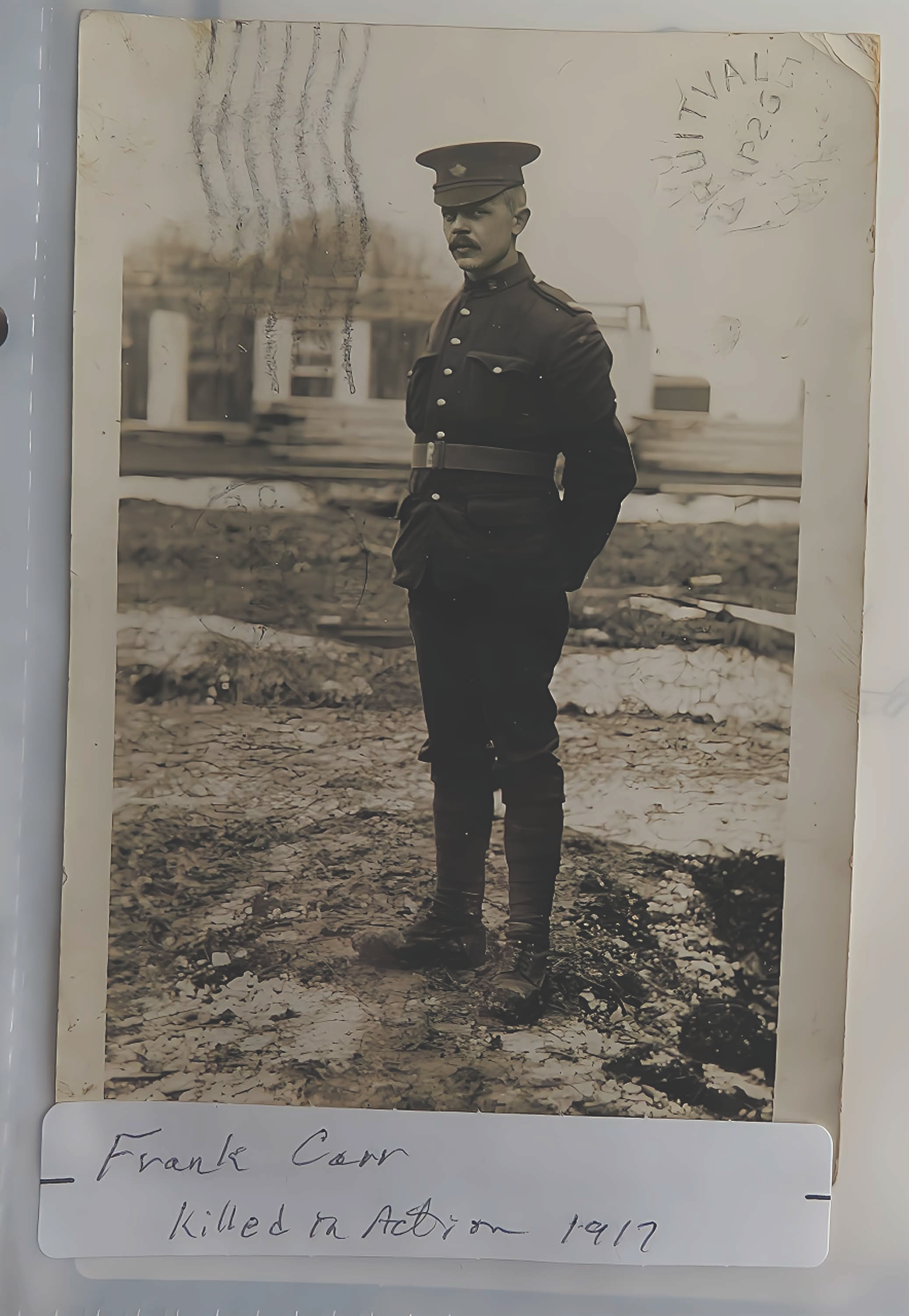 A black and white historical photograph of a young man in a military uniform, standing outdoors on rough ground. The photo has a handwritten caption at the bottom that says: "Frank Cown killed in Action 1917." There is also some writing on the top right corner and faint marks across the image.