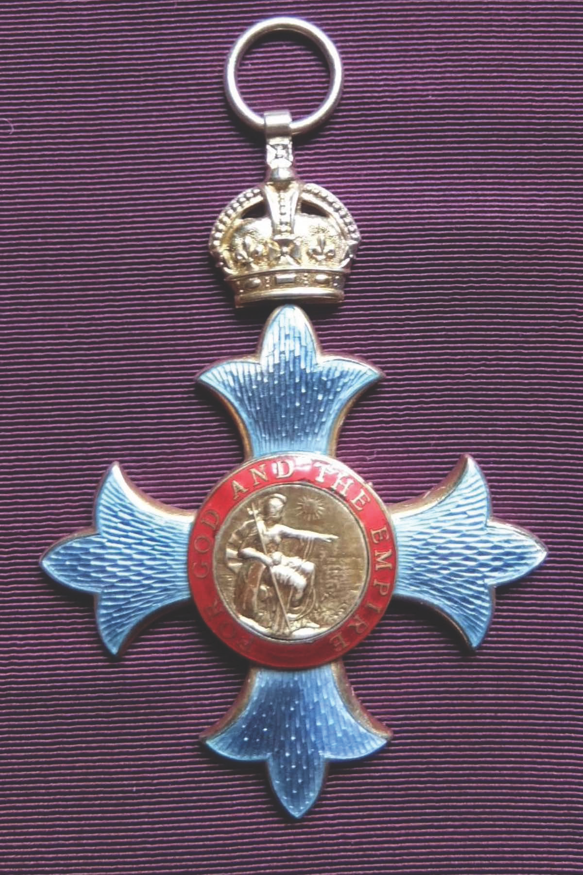 A medal with a crown at the top, a central circular emblem with a seated figure pointing, surrounded by red text reading 'GOD AND THE EMPIRE,' and a decorative star-shaped silver background.