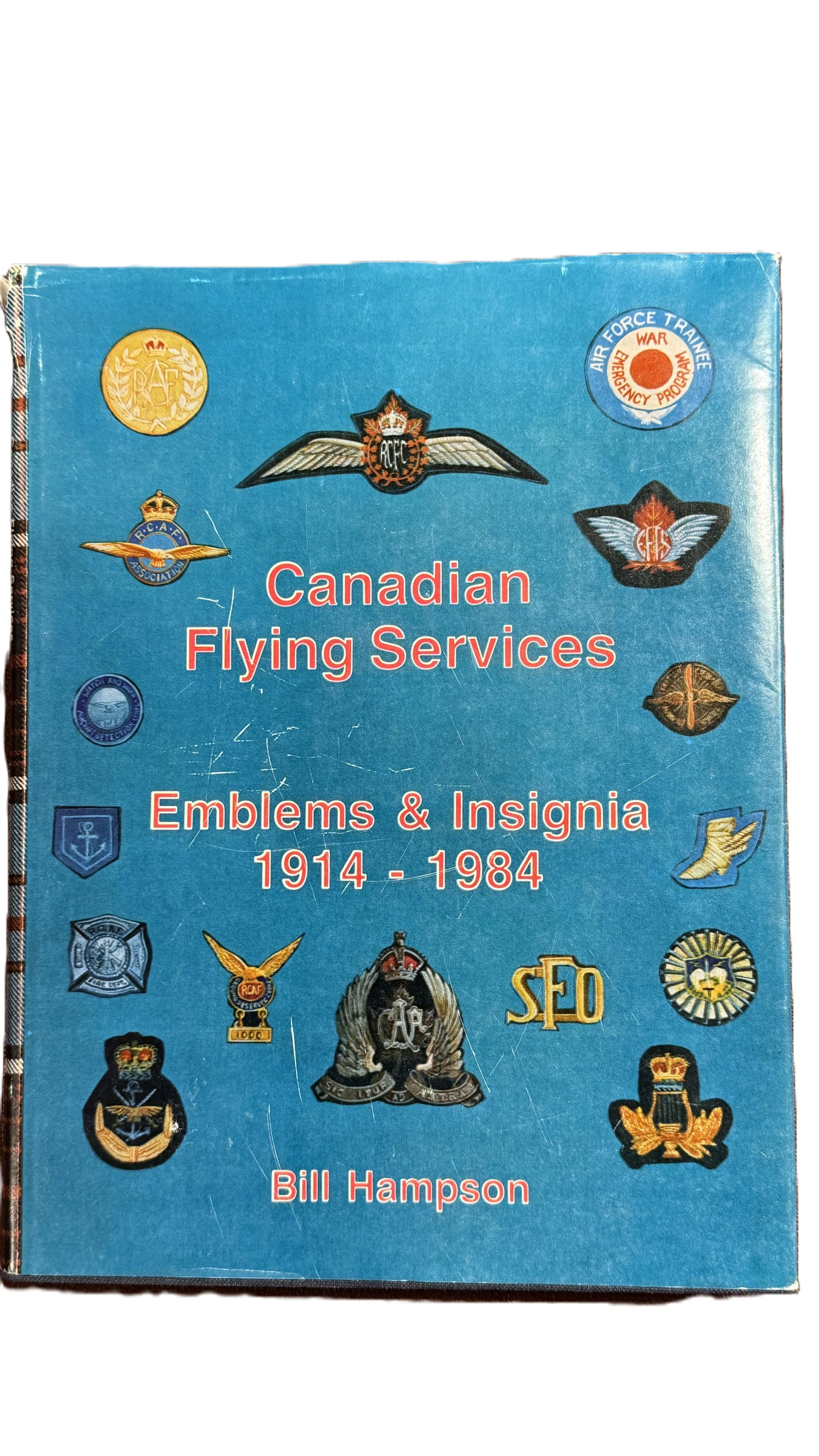 Book titled 'Canadian Flying Services Emblems & Insignia 1914 - 1984' by Bill Hampson, featuring various military insignia and patches on a blue background.