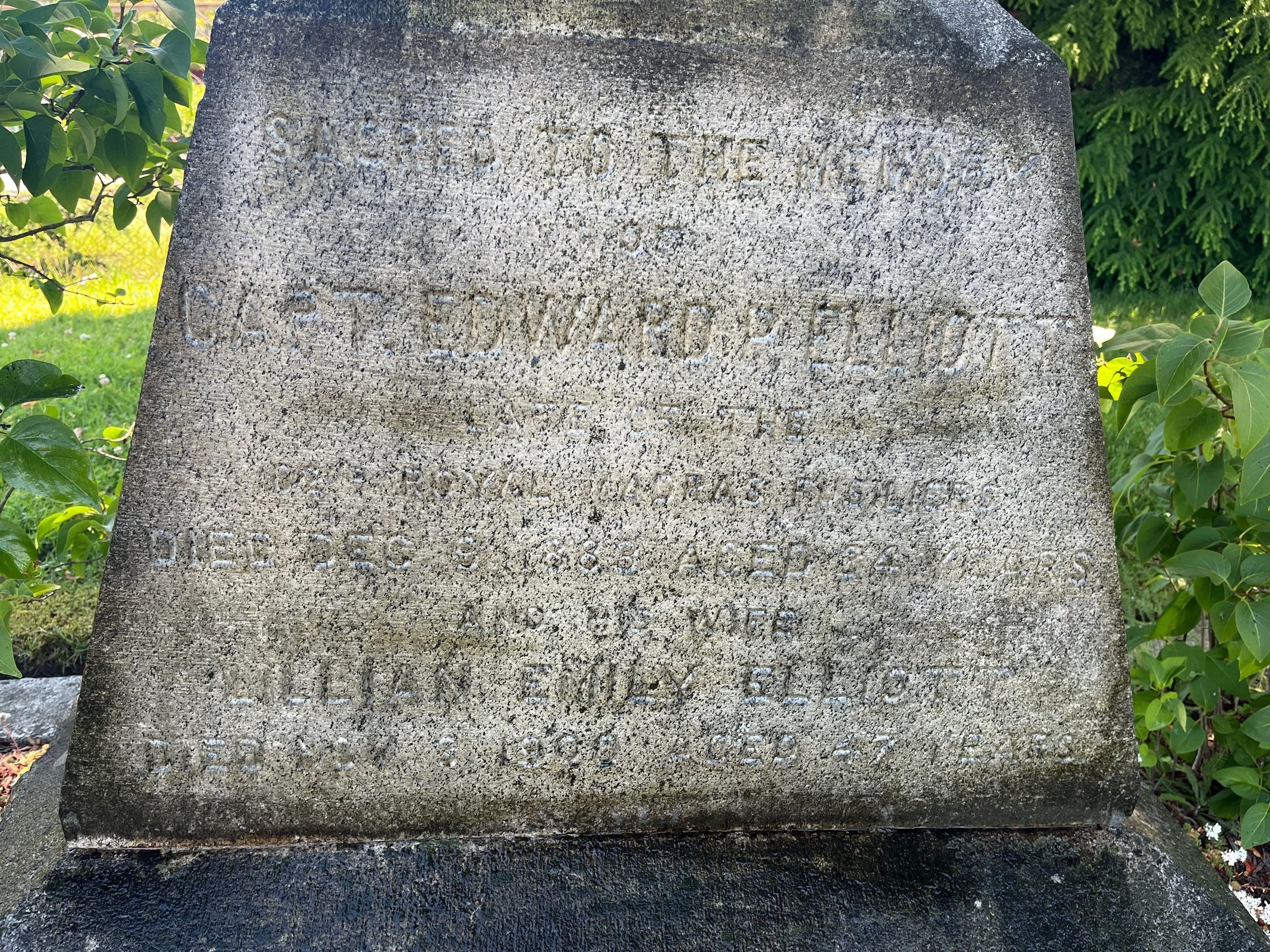 A weathered stone memorial with engraved text, surrounded by green foliage, commemorating someone who was born in 1891 and died in 1960.