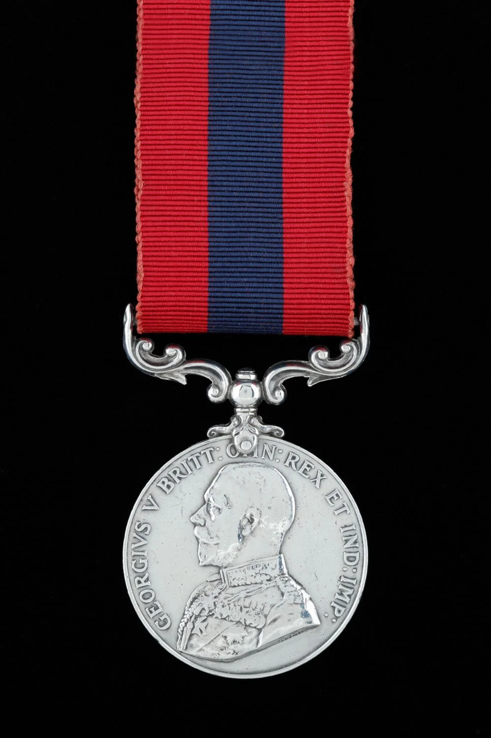 A military medal with a red and blue striped ribbon and a silver medallion featuring the profile of King George V and an inscription in Latin.