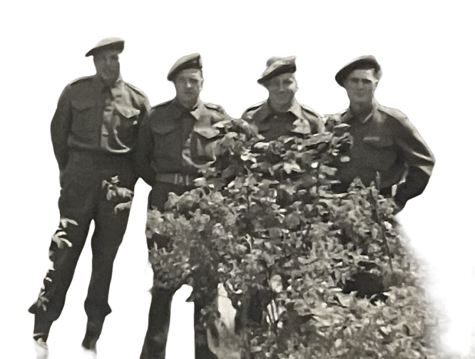 Four soldiers stand outdoors next to a large bush or tree, posing for the photograph.