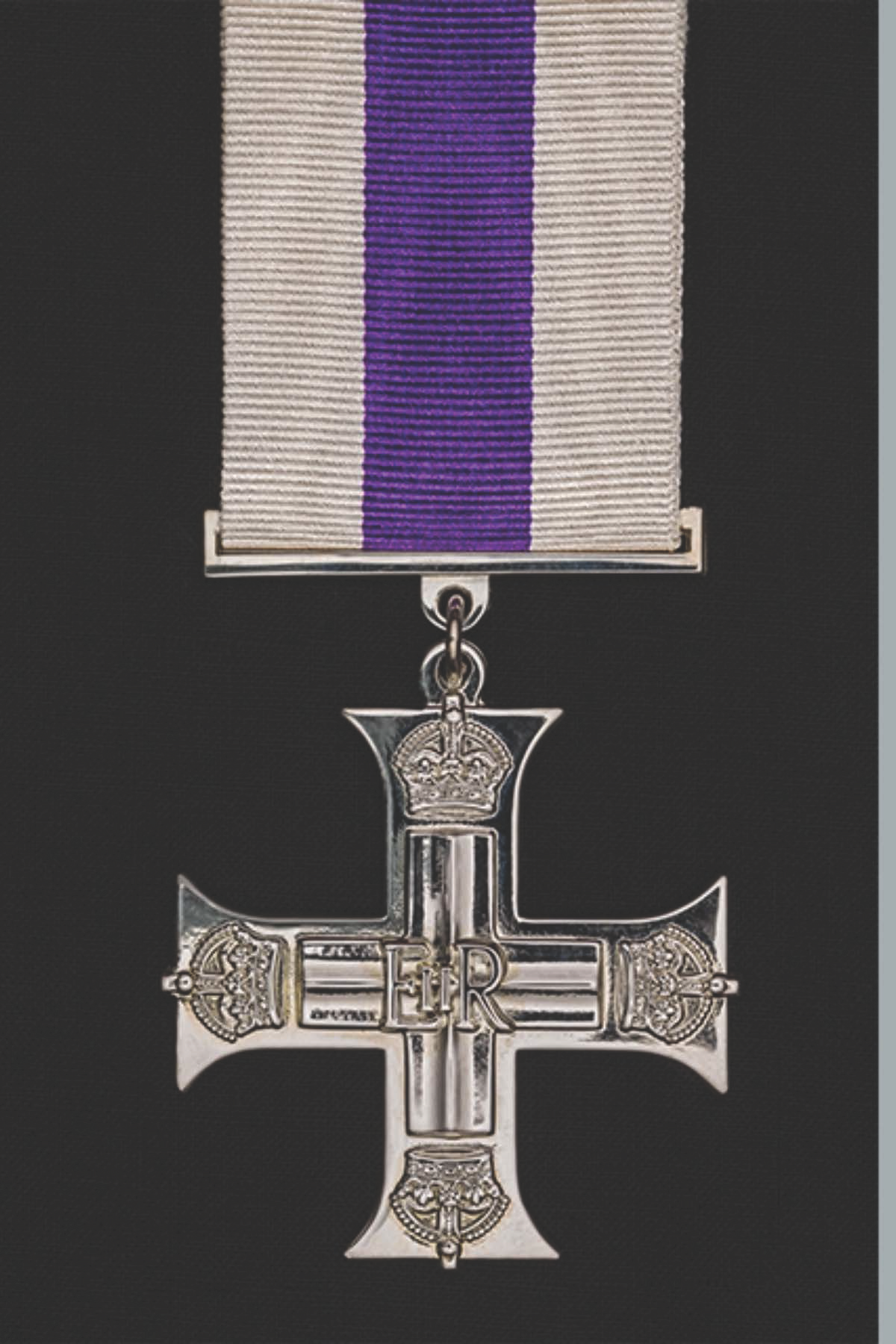 A silver medal in the shape of a cross with a crown on top and the letters 'E R' in the center, hanging from a purple and white ribbon.