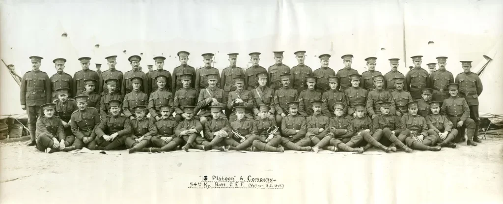 A black-and-white photograph of a large group of soldiers in uniform, posing outdoors against a plain background. The soldiers are arranged in four rows, with some seated on the ground and others standing. The text below the group reads, '8 Platoon A