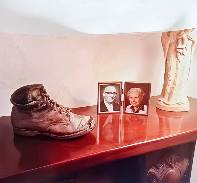Decorative display on a wooden surface including an old boot, two framed photographs of a man and woman, and a ceramic sculpture of a face.
