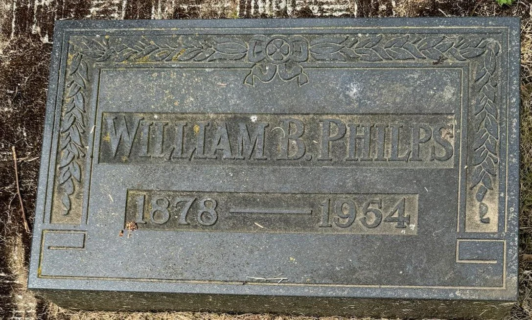 Metal grave marker for William B. Phillips, from 1878 to 1954, with decorative border including flowers and leaves.