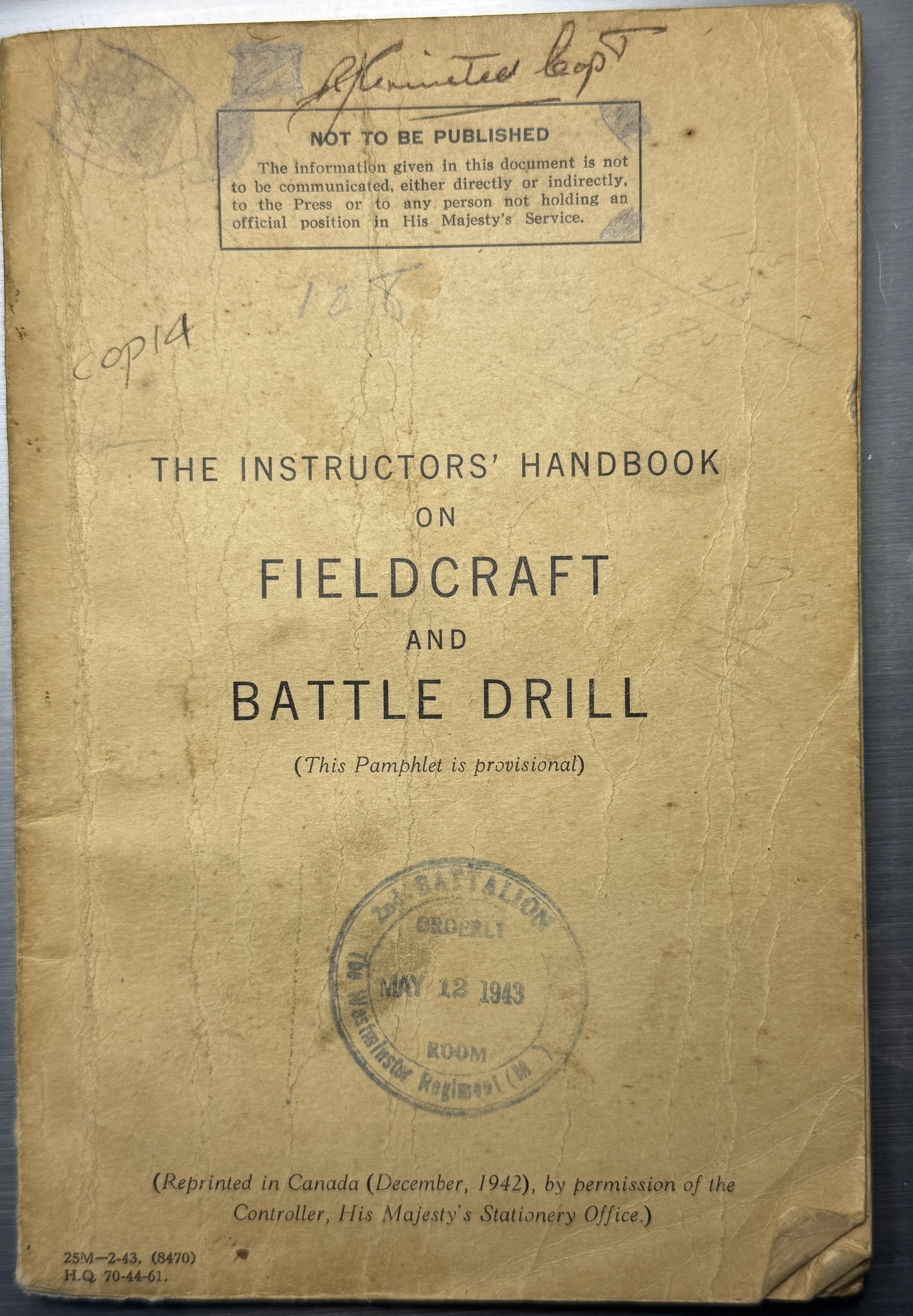 Old, worn booklet titled "The Instructors' Handbook on Fieldcraft and Battle Drill" dated May 12, 1943, with a government stamp and handwritten notes on the cover.