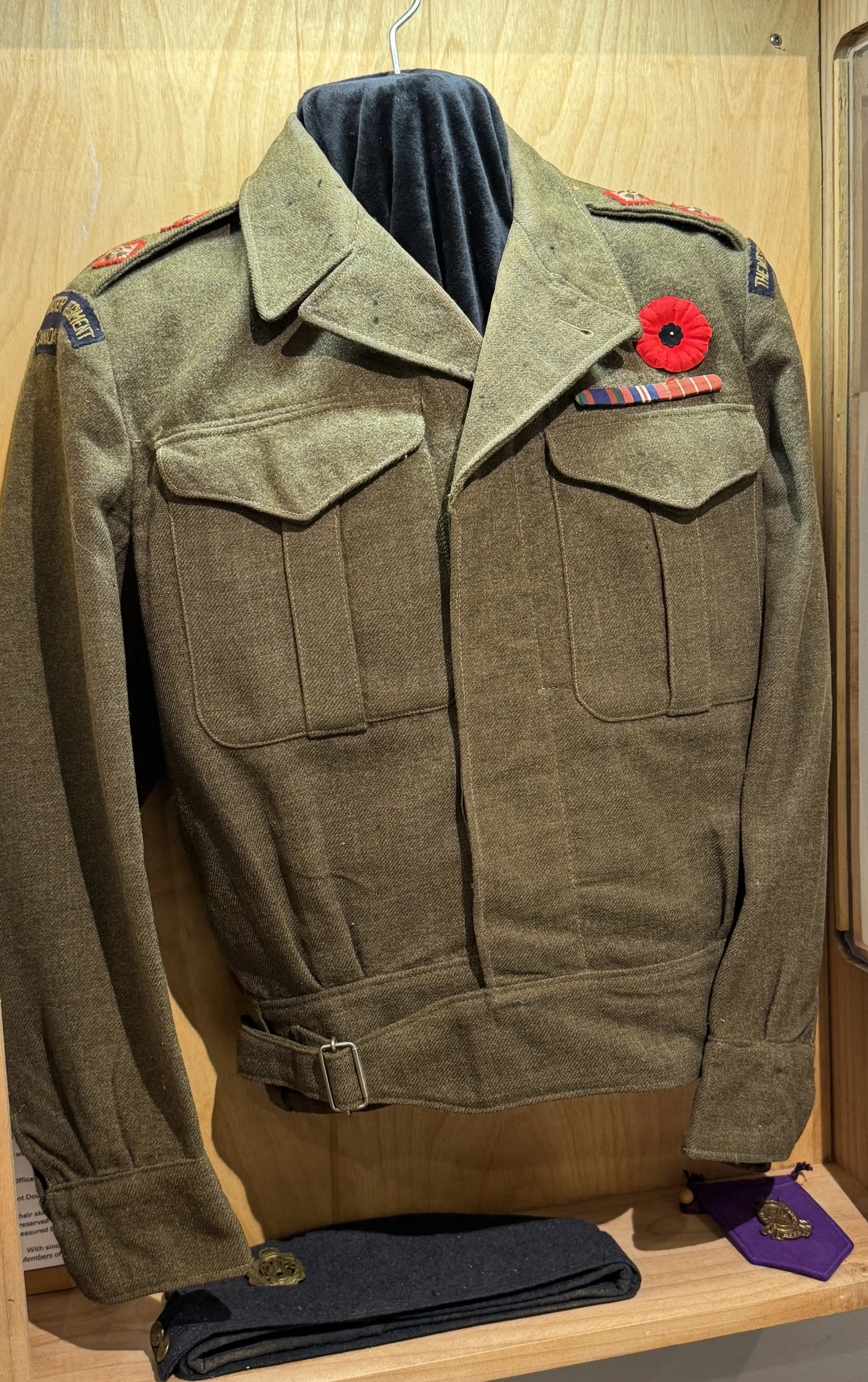 World War II military uniform displayed on a hanger, with a red poppy pin, medal ribbons, and various insignia