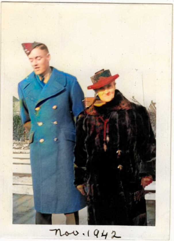 A young man and woman dressed in vintage clothing from November 1942, standing outdoors with a white fence behind them.