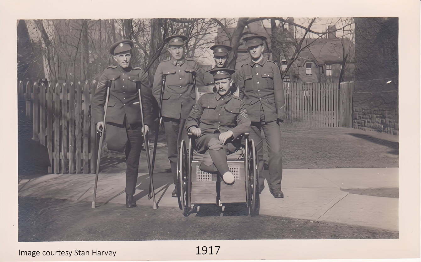 Black and white historical photograph from 1917 showing five military personnel, four women standing and a man in a wheelchair seated in front. They are outdoors, near a wooden fence and trees, dressed in early 20th-century military uniforms.