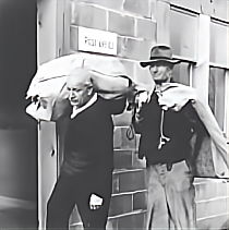 Two men in suits and hats walking outside a brick building with a sign that reads 'POLICE'.