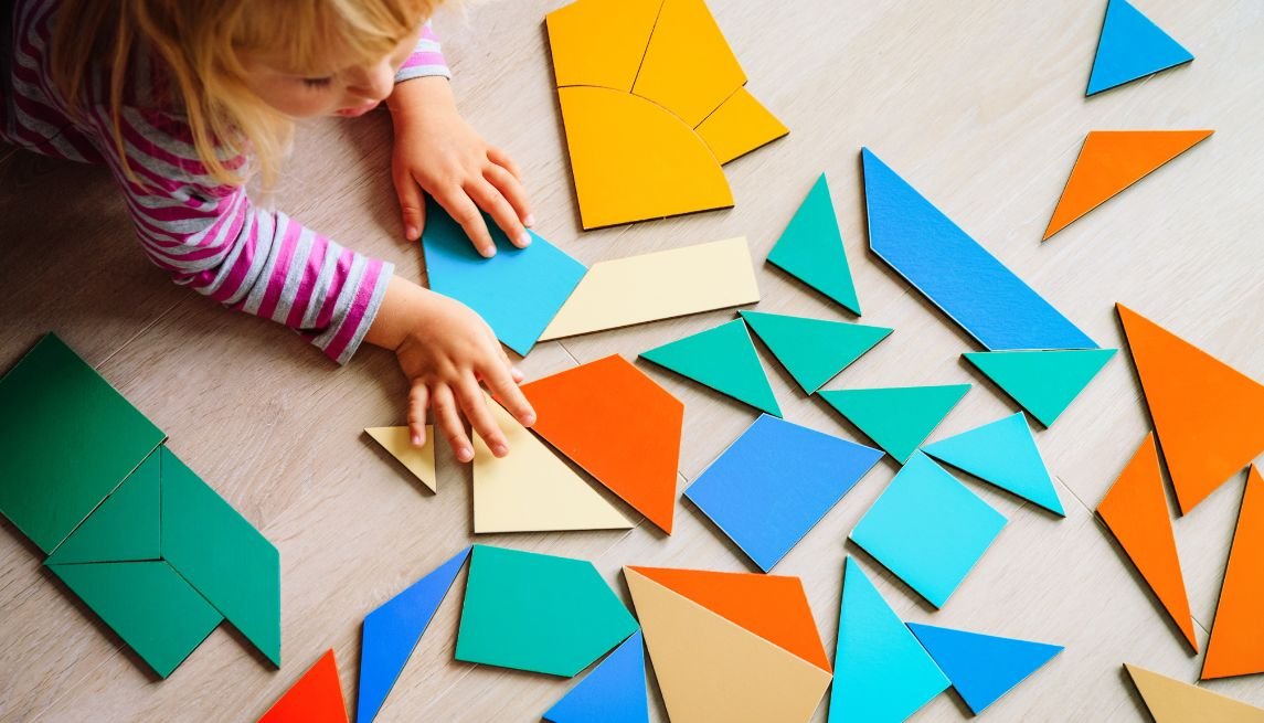 Young child playing with colorful geometric shape puzzles on the floor.