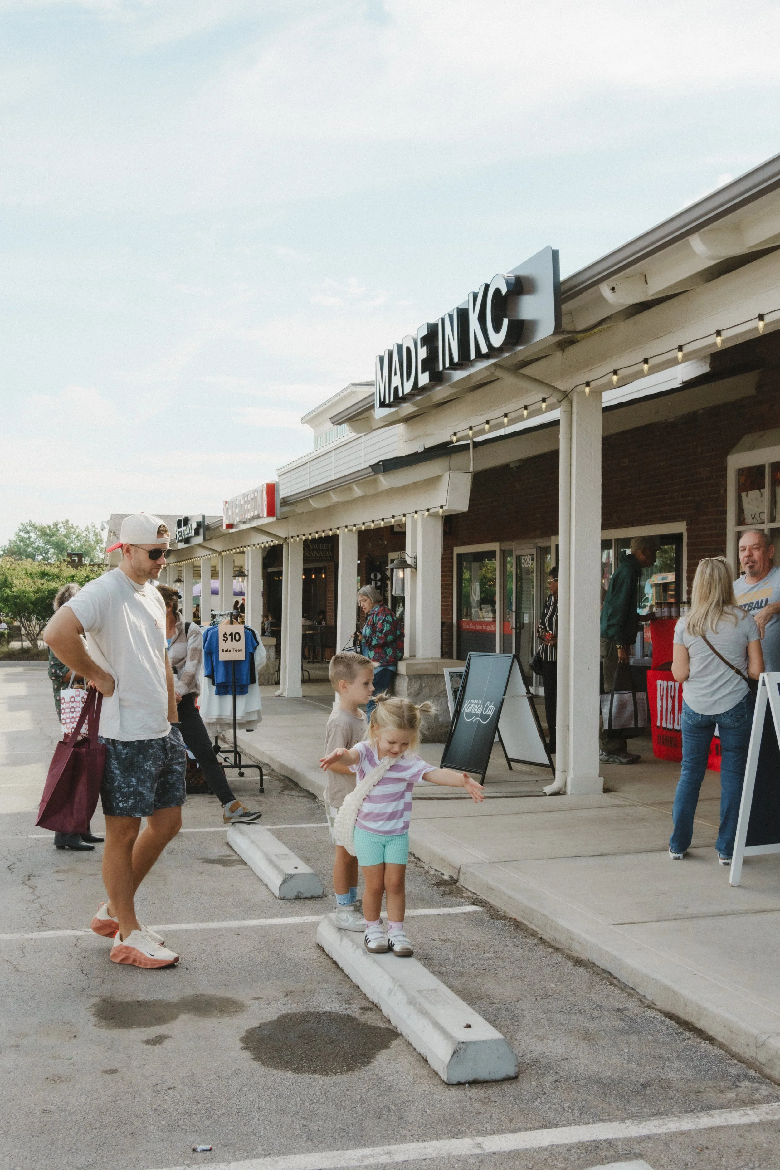 People standing and walking outside a store with a sign that reads 'Made in KC' during daytime.