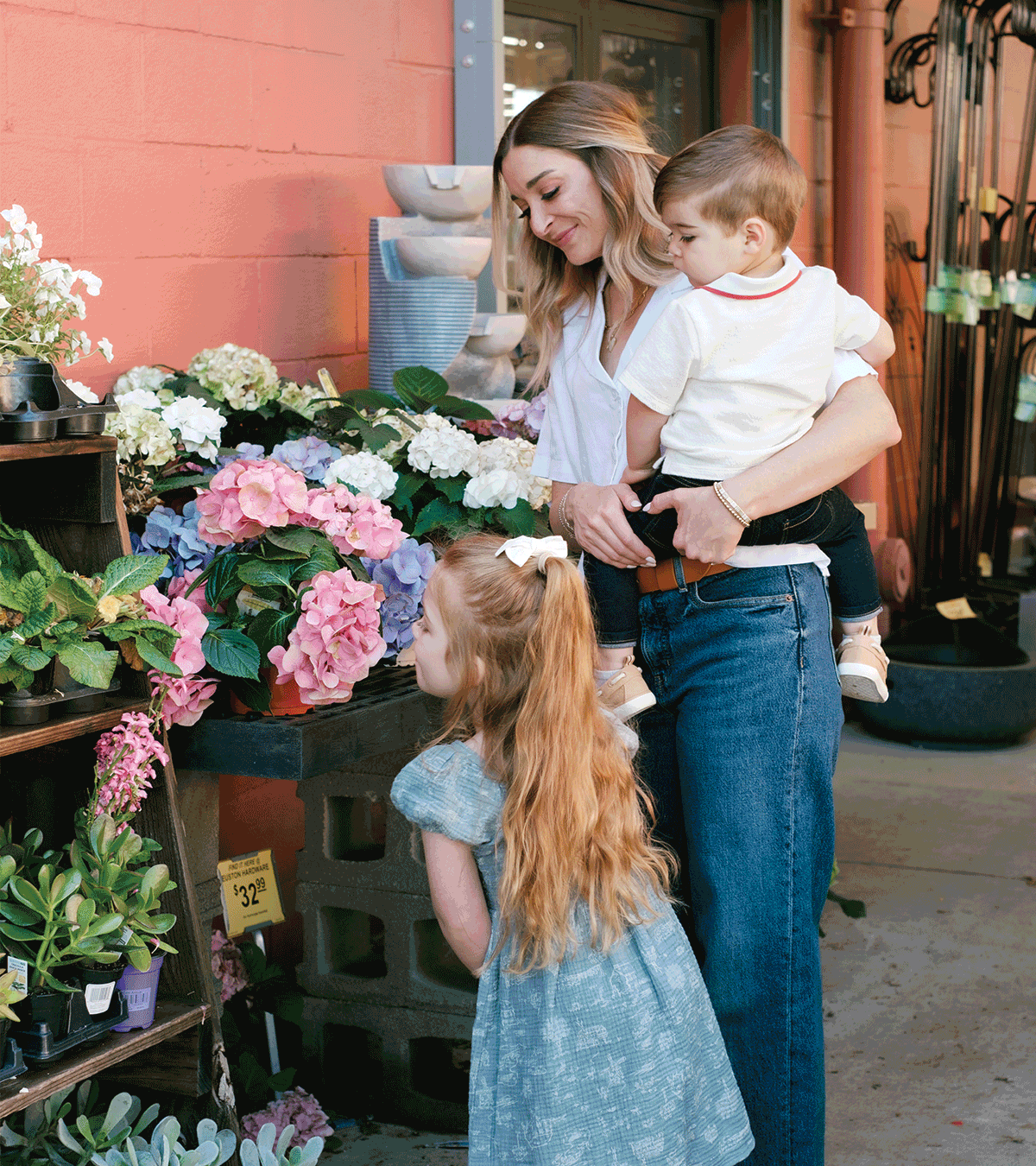 A woman with two young children shopping for flowers at a plant store.