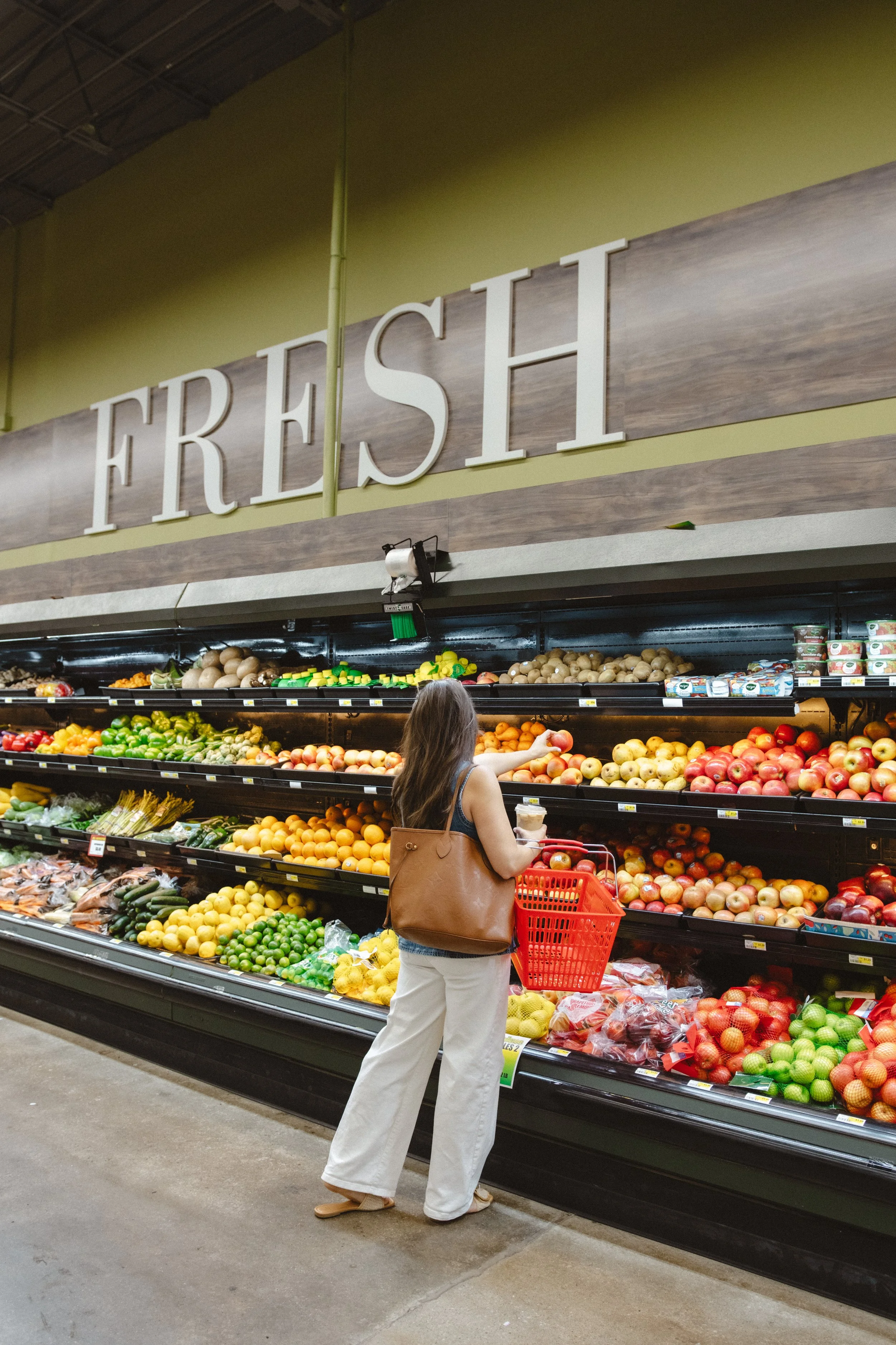 A woman shopping for fruits in a grocery store's produce section marked 'FRESH'.